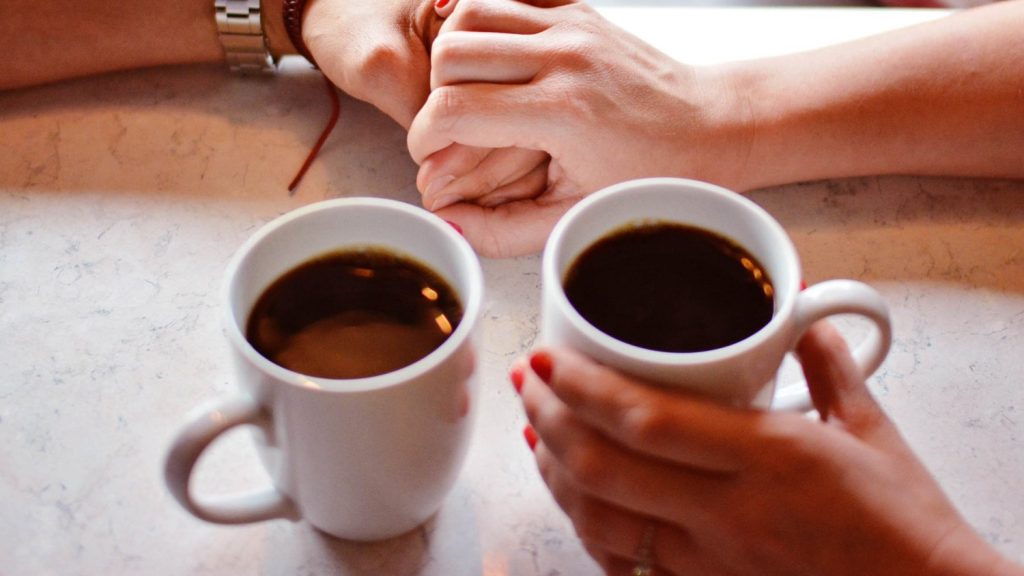 Deux mains qui se tiennent devant deux tasses à café.