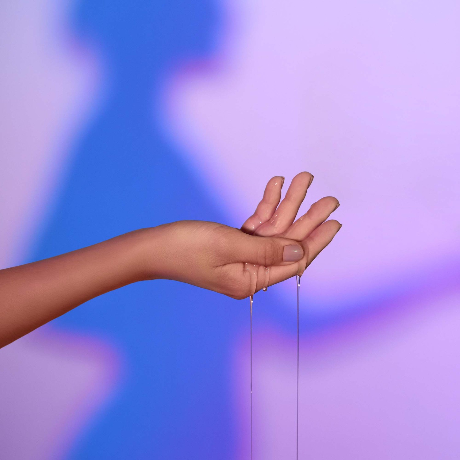 Main avec du lubrifiant qui coule, derrière silhouette de femme en ombre.